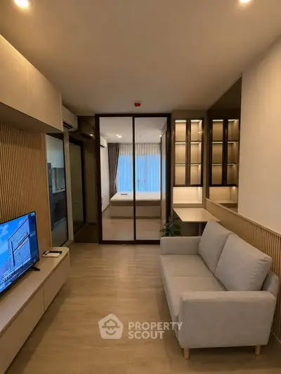 Modern living room with cozy sofa and TV, leading to a stylish bedroom with glass partition.