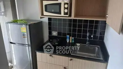 Modern compact kitchen with microwave, fridge, and sleek black tile backsplash.