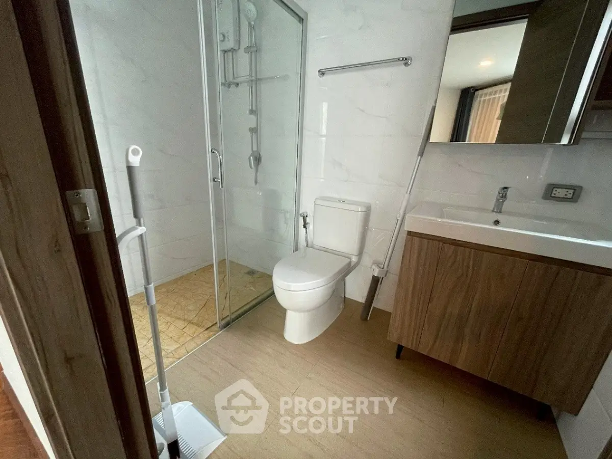Modern bathroom with glass shower and wooden vanity in sleek apartment.