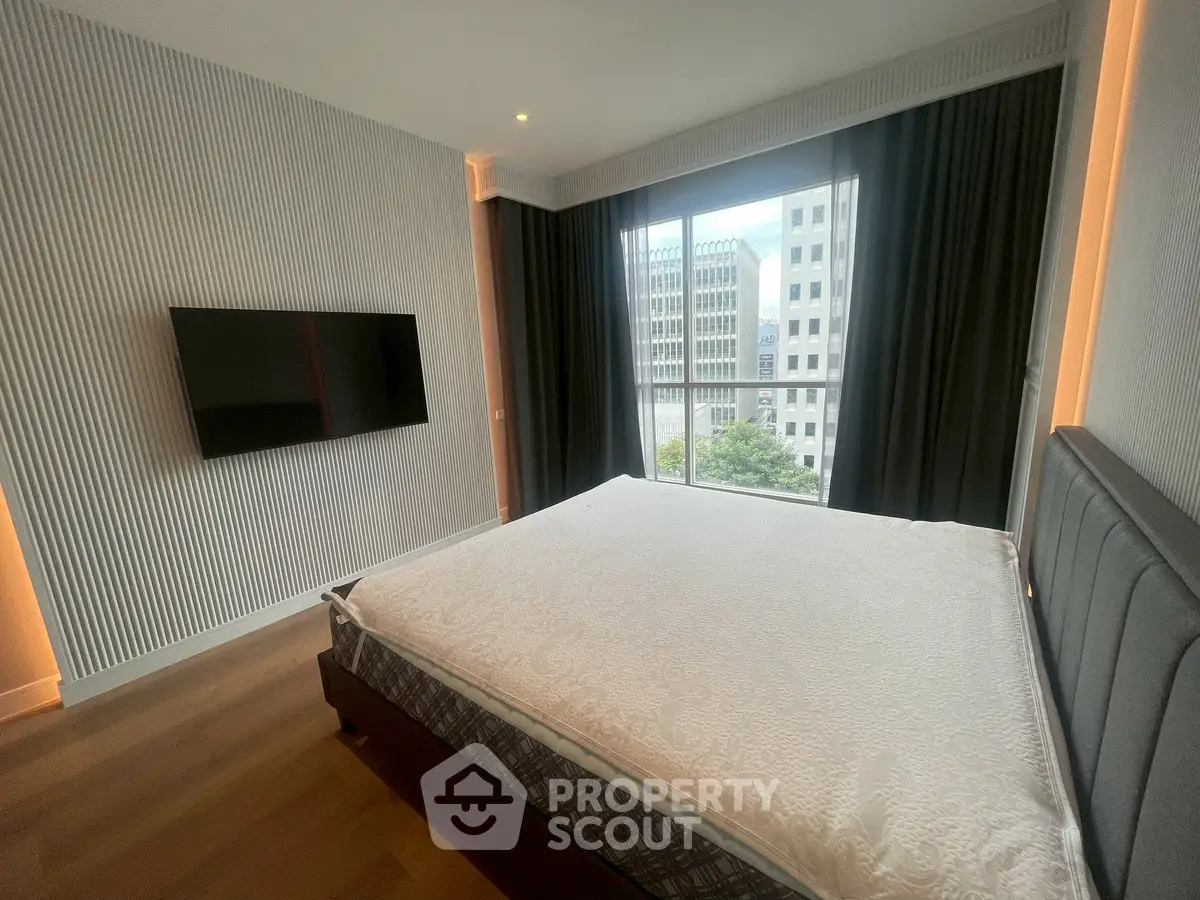 Modern bedroom with large window and city view, featuring a wall-mounted TV and stylish decor.