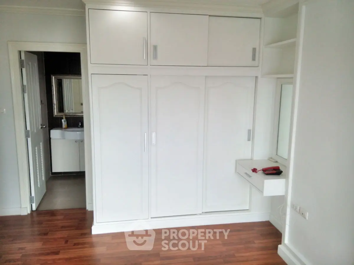 Spacious bedroom with built-in white wardrobe and wooden flooring