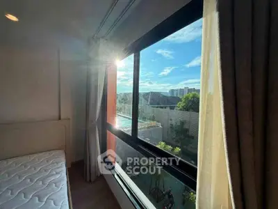 Bright bedroom with large window offering stunning city view and natural light.