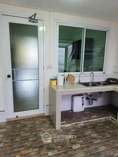 Spacious kitchen with dual sinks and modern tiled flooring, featuring a glass door and ample natural light.