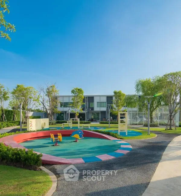 Modern residential complex with vibrant playground and lush greenery under clear blue sky.