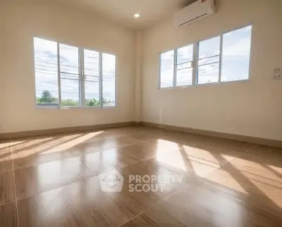 Spacious sunlit room with large windows and polished wooden floors, perfect for a cozy living space.