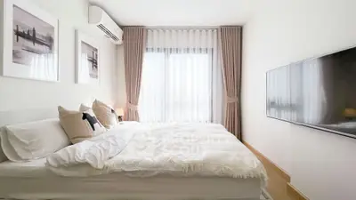 Modern bedroom with cozy bed, wall-mounted TV, and elegant curtains in a bright apartment.
