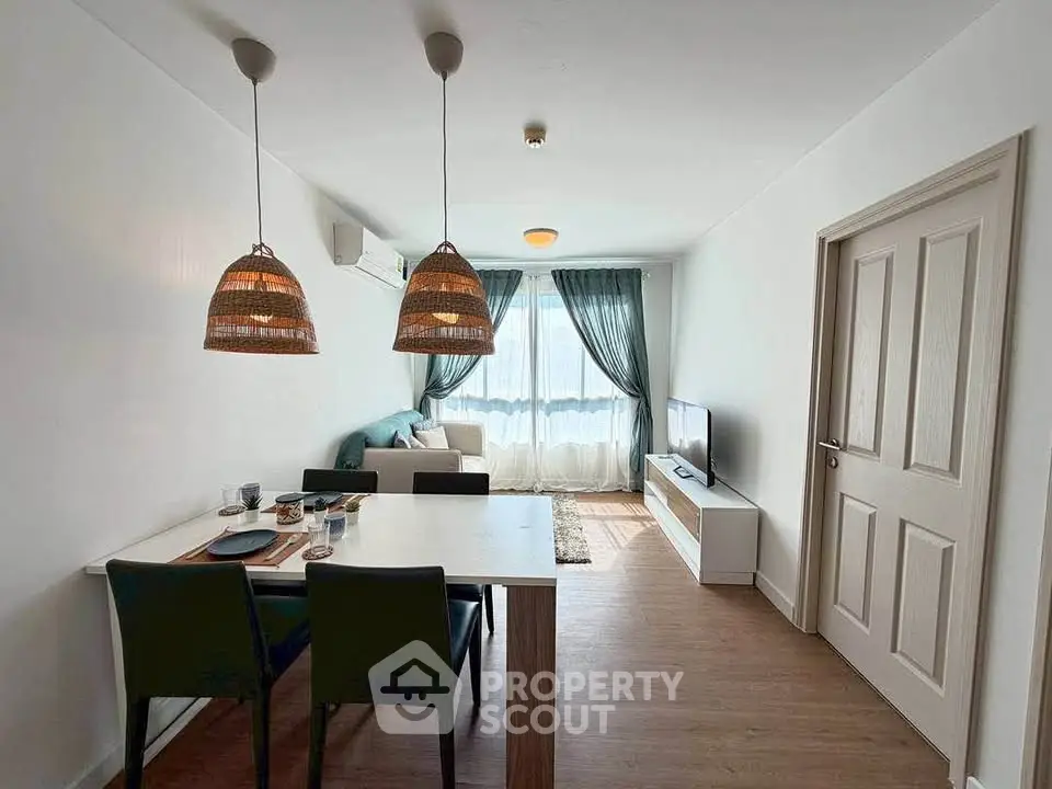 Modern living room with dining area, stylish lighting, and natural light from large window.