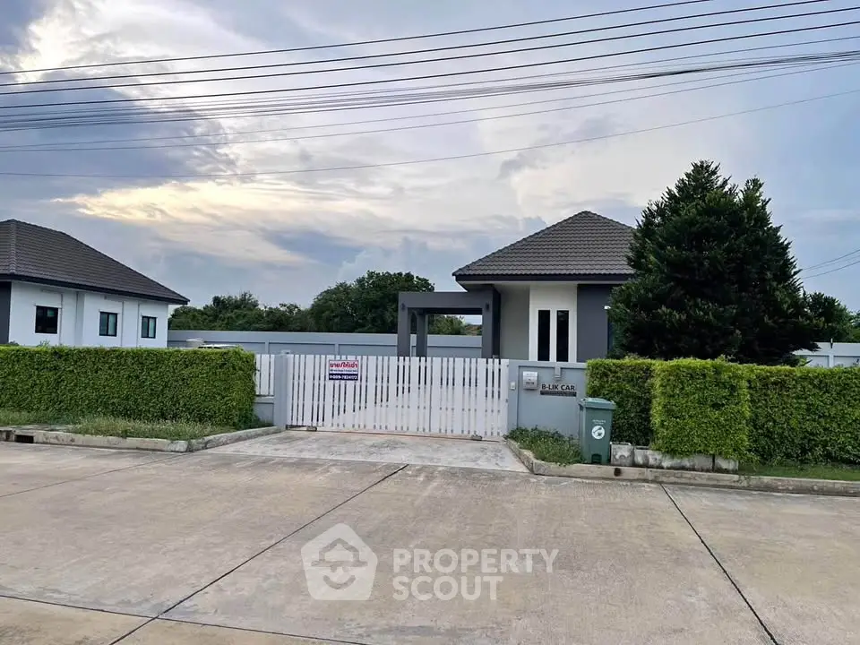 Modern single-story house with gated entrance and lush greenery in a serene neighborhood.