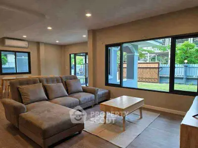 Spacious modern living room with large windows and stylish furniture, offering a serene garden view.