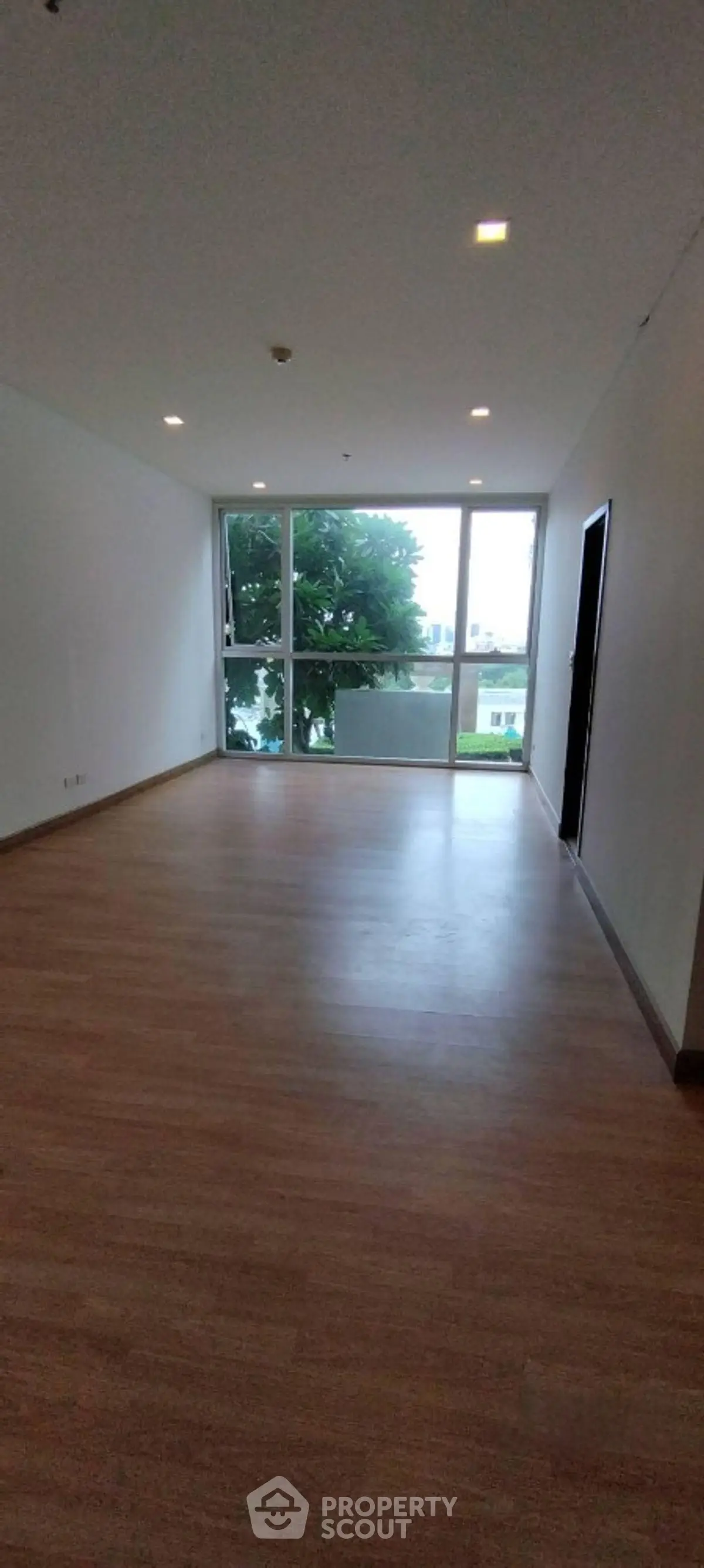 Spacious empty living room with large window and wooden flooring