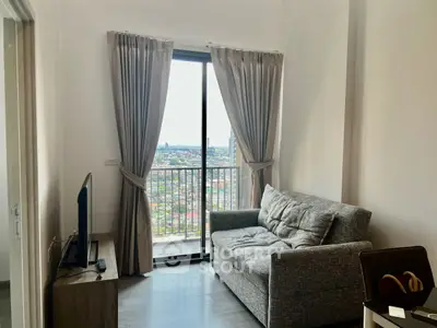 Modern living room with balcony and stunning city view, featuring cozy gray sofa and sleek TV setup.