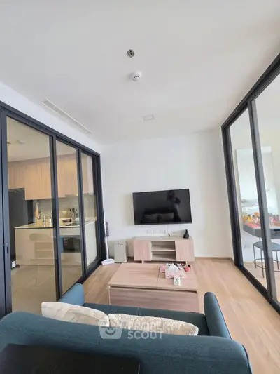 Modern living room with sleek furniture and open kitchen layout, featuring large glass doors and stylish decor.