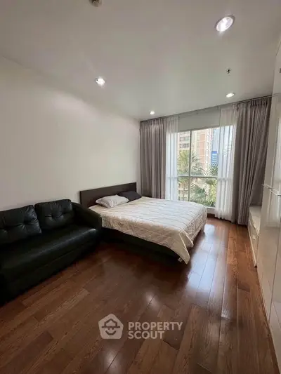 Spacious bedroom with wooden flooring and large window offering city views
