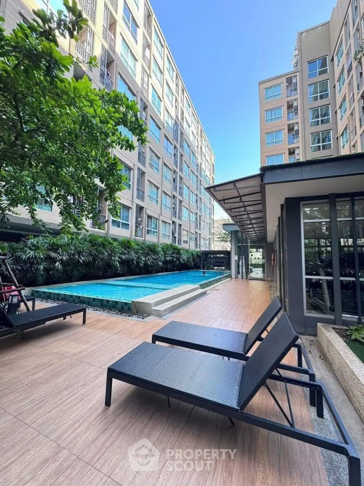 Modern apartment complex with pool and lounge chairs, perfect for relaxation.