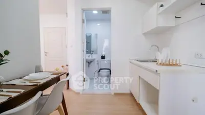 Modern compact kitchen and dining area with adjacent bathroom in minimalist apartment.