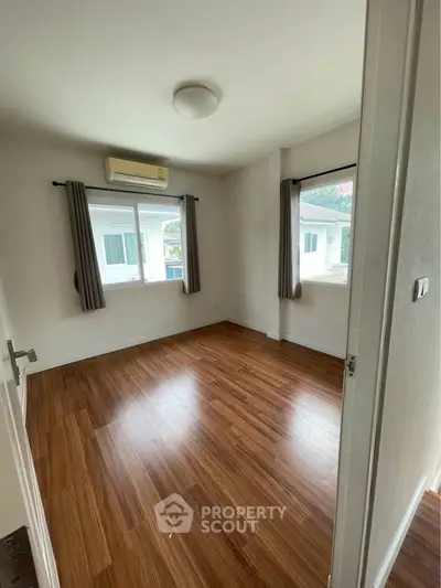 Spacious empty room with wooden flooring and large windows in modern home.