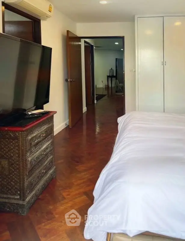 Spacious bedroom with elegant wooden flooring and large TV, perfect for relaxation.