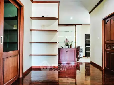 Elegant interior with polished wooden floors and built-in shelves, leading to a dining area with classic wooden cabinetry.