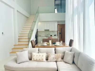 Modern loft apartment with open kitchen and stylish living area, featuring elegant staircase and natural light.