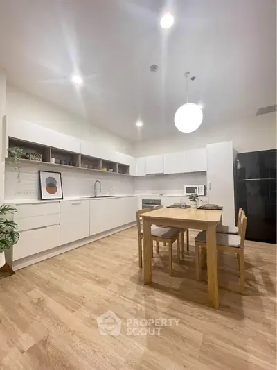 Modern kitchen with sleek white cabinets and wooden dining table in spacious open layout.