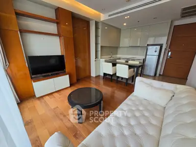 Modern living room with open kitchen, featuring sleek furniture and wooden flooring.