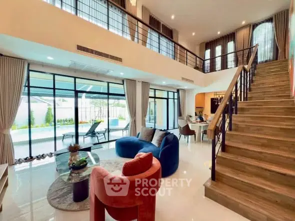 Luxurious modern living room with high ceilings, elegant staircase, and large windows overlooking a garden.
