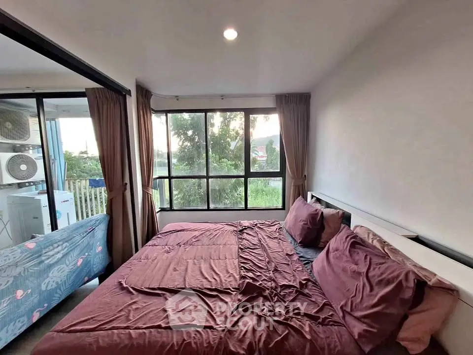 Cozy bedroom with large windows and lush outdoor view, featuring a comfortable bed and elegant curtains.