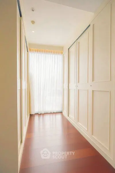 Bright hallway with elegant wooden flooring and large windows with sheer curtains.