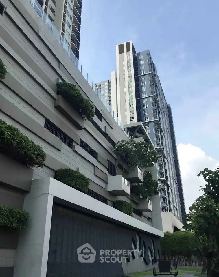 Modern high-rise building with unique architectural design and lush greenery in urban setting.