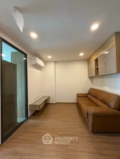 Modern living room with leather sofa and wooden flooring, featuring a sleek glass partition and built-in storage.