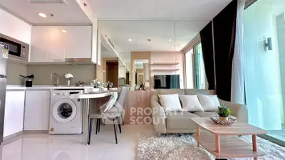 Modern living room with open kitchen, washing machine, and cozy seating area in a bright apartment.