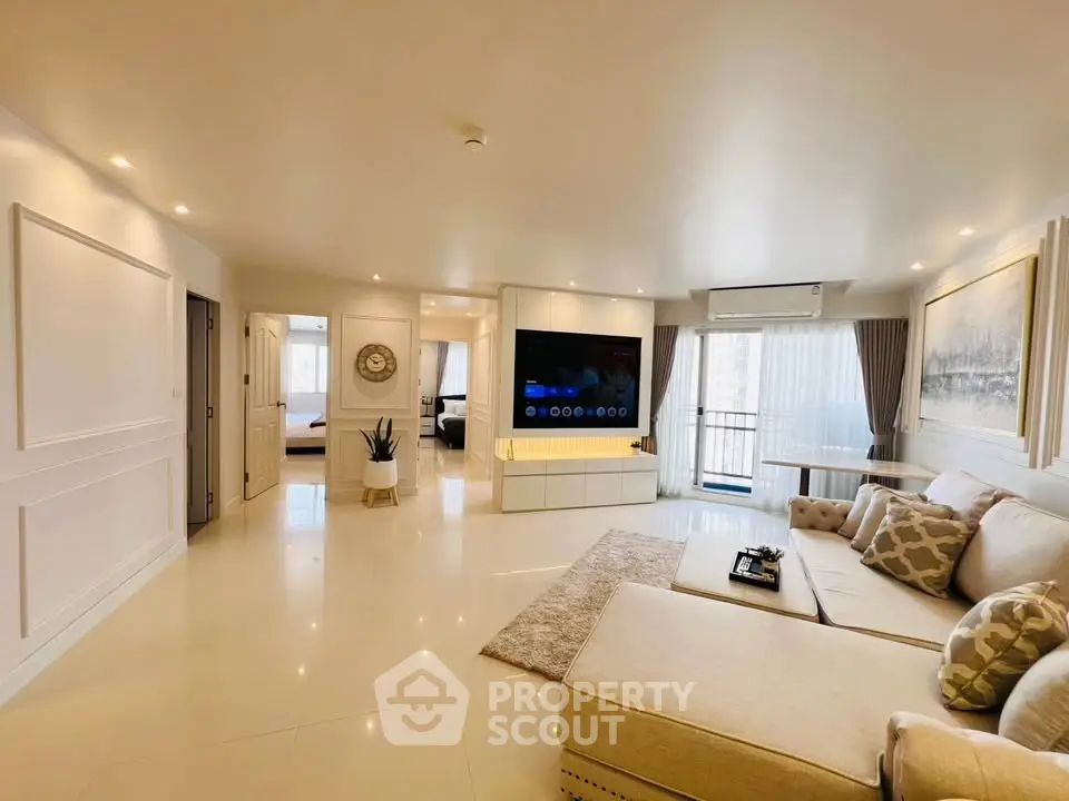 Spacious modern living room with elegant decor and large TV, leading to a bright bedroom.