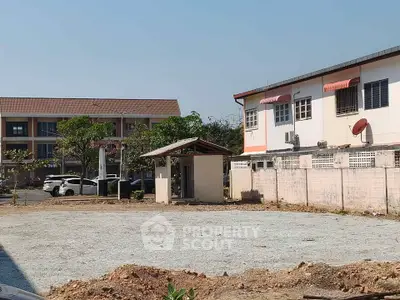 Vacant land plot with potential for development in a residential area, featuring nearby buildings and parking.