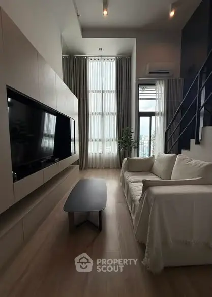 Modern living room with high ceilings and large windows, featuring a sleek TV setup and cozy sofa.