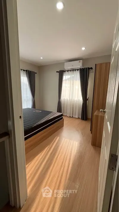 Cozy bedroom with wooden flooring, large windows, and modern air conditioning unit.