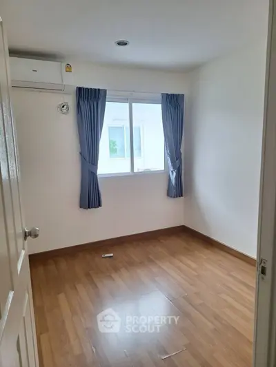 Bright empty room with wooden flooring and blue curtains, ideal for customization.