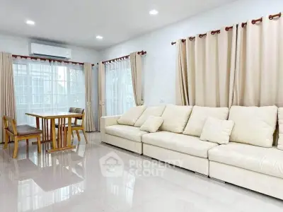 Spacious living room with elegant beige sofa and dining area, featuring large windows and natural light.