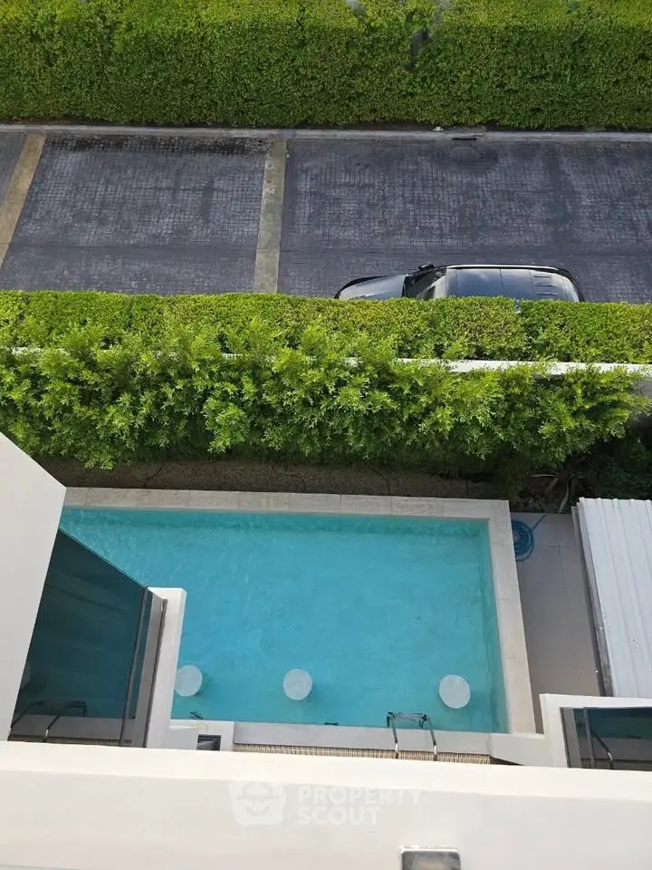 Stunning aerial view of a private pool with lush greenery and parking area, perfect for relaxation and leisure.