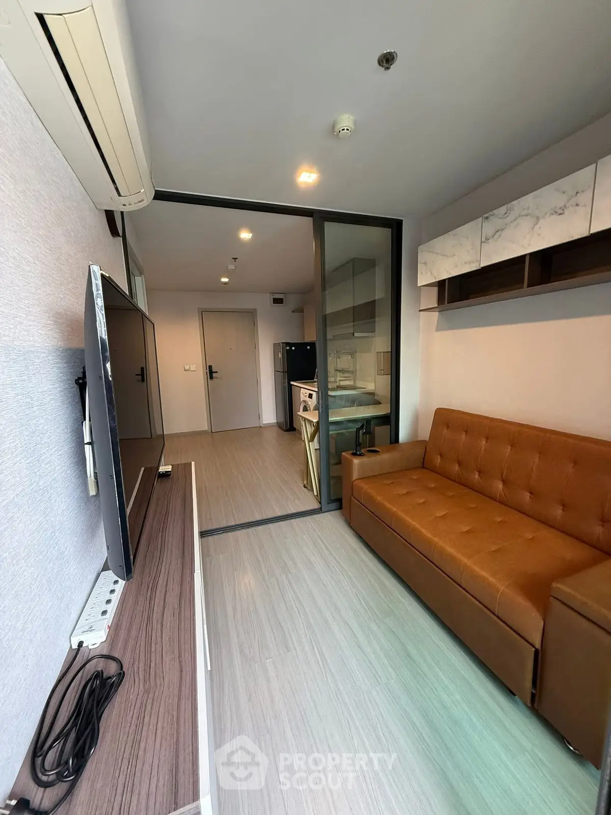 Modern living room with brown leather sofa and large TV, open layout to kitchen