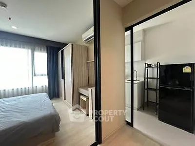 Modern apartment with bedroom and compact kitchen, featuring sleek design and natural light.