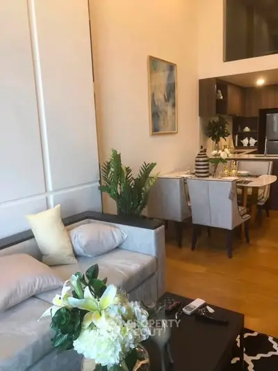 Elegant living room with modern decor and open kitchen layout, featuring stylish furniture and vibrant plants.