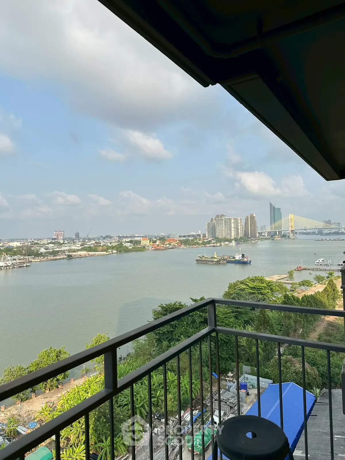 Stunning river view from a high-rise balcony with lush greenery and cityscape in the background.