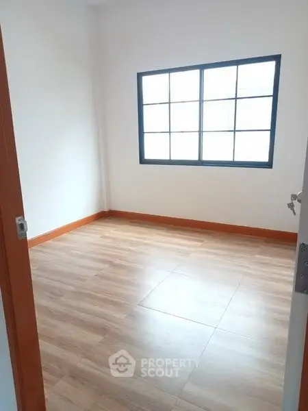 Spacious empty room with wooden flooring and large window, perfect for customization.