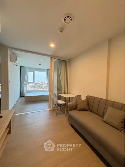 Modern living room with cozy sofa and view into a bright bedroom