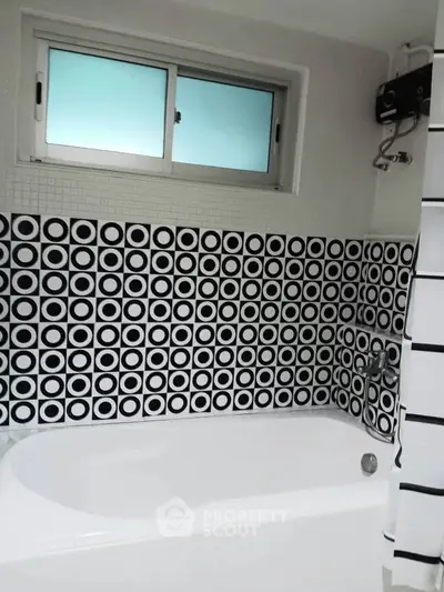 Stylish bathroom with modern black and white circular tile design and bathtub.