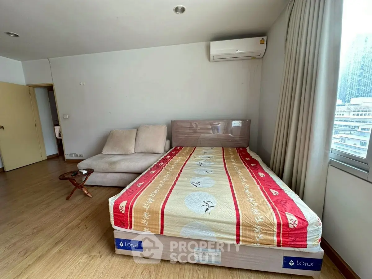 Spacious bedroom with modern decor and city view, featuring a cozy bed and stylish sofa.