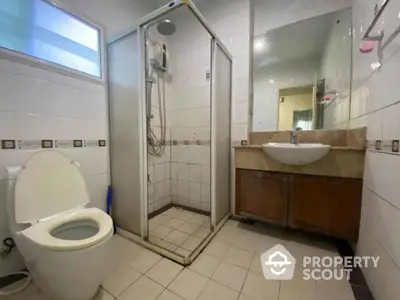 Spacious bathroom with modern fixtures, including a glass shower cubicle, wall-mounted sink, and large mirror, reflecting a well-lit and clean space.