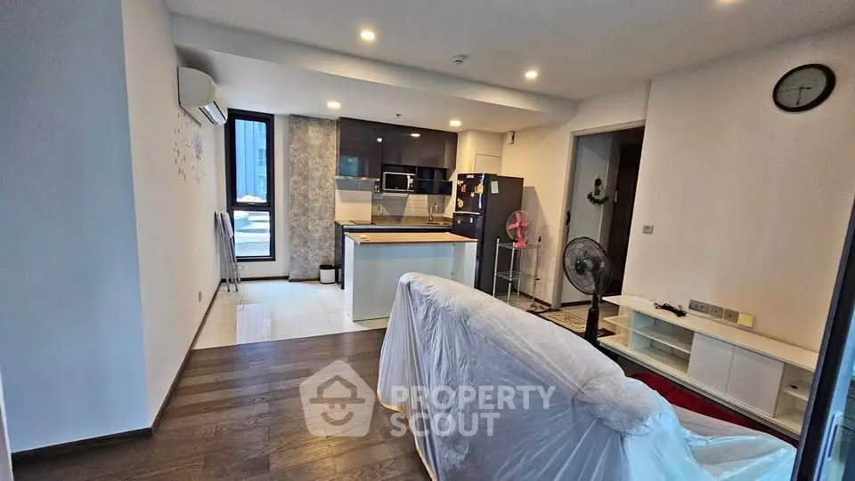 Modern open-layout living room with kitchen, featuring sleek design and ample natural light.