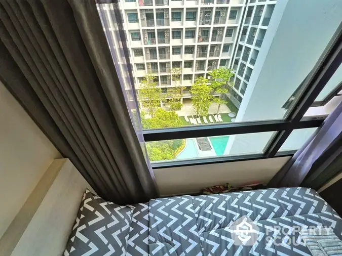 Cozy bedroom with a stunning view of the pool and lush garden, offering a serene urban retreat in a modern high-rise apartment complex.