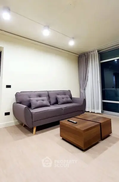 Modern living room with stylish sofa and wooden coffee table, featuring elegant lighting and large window.